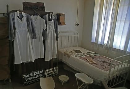 Eingerichtetes Patientenzimmer mit Eisenbett und Arztkittel