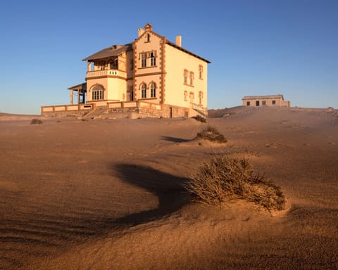 Villa in Kolmanskop im warmen Abendlicht mit Dünen