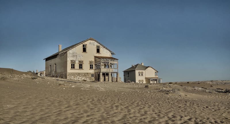 Verlassene Häuser von Kolmanskop im Sand unter grauem Himmel