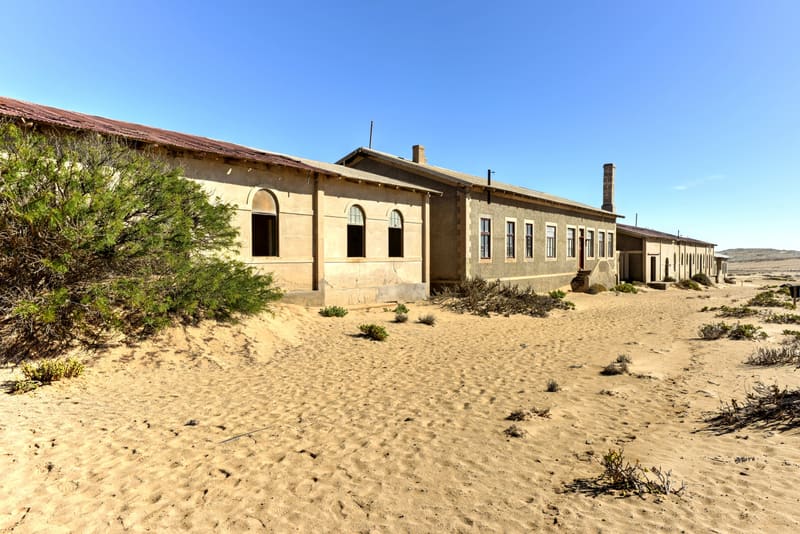 Lange Häuserzeile von Kolmanskop mit Dünen im Vordergrund